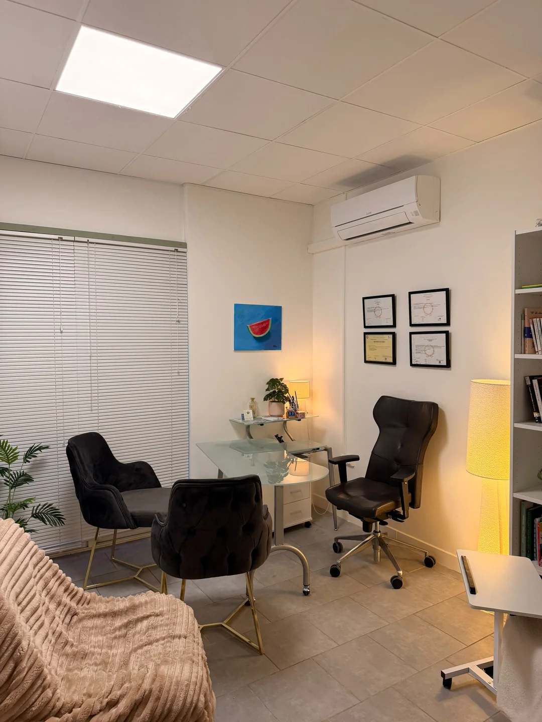 Le bureau en verre et les fauteuils noirs, éclairés par deux lampes au cabinet.