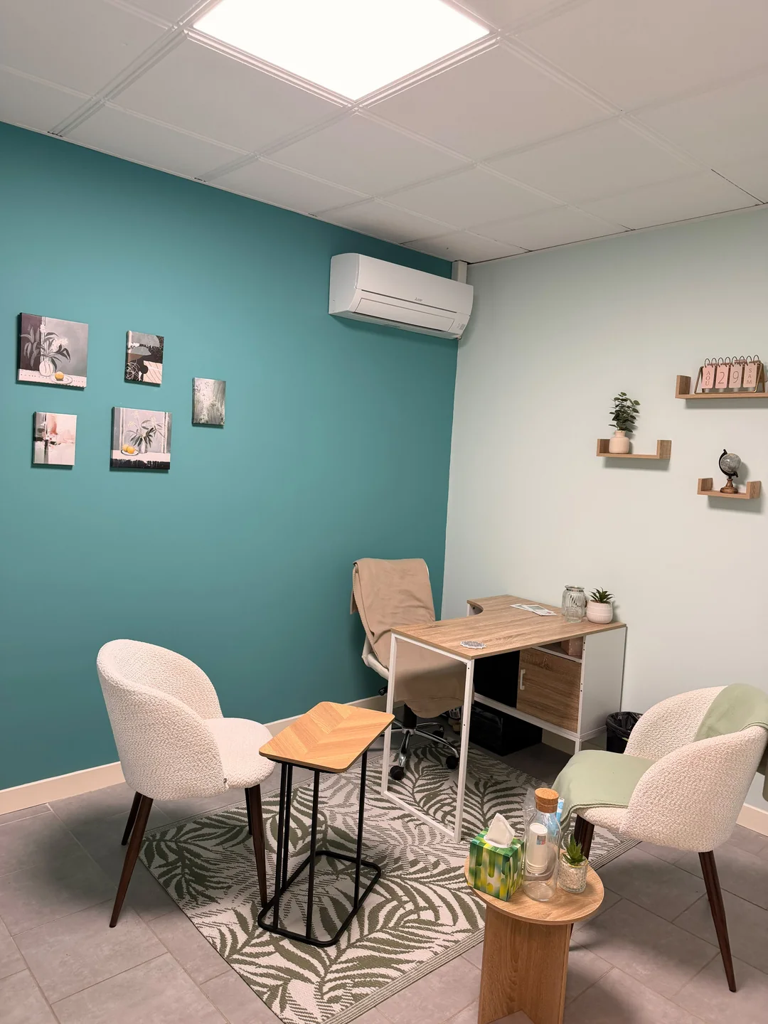 Une pièce aux murs turquoise, avec un bureau en bois et deux fauteuils clairs.